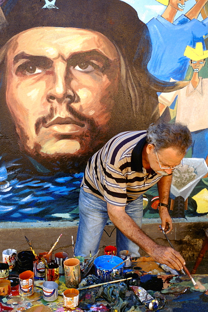 An artist painting a wall mural featuring a portrait of the revolutionary hero Che Guevara on a street in Baracoa, Cuba