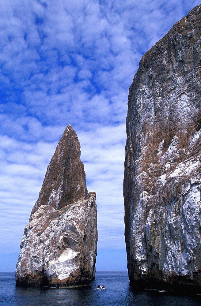 A dive boat passes between two spectacular volcanic plugs called Kicker Rock, located off San Cristobal Island, Galapagos Islands, Ecuador