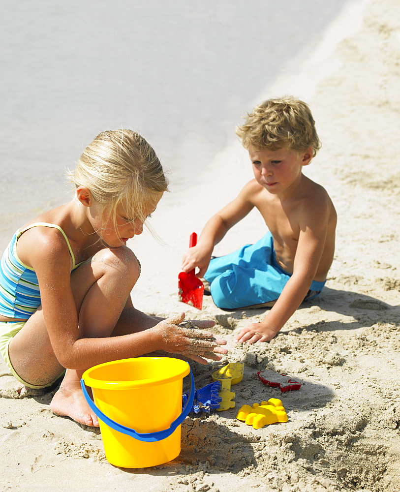 Boy and girl (6-8) on beach making sandcastles