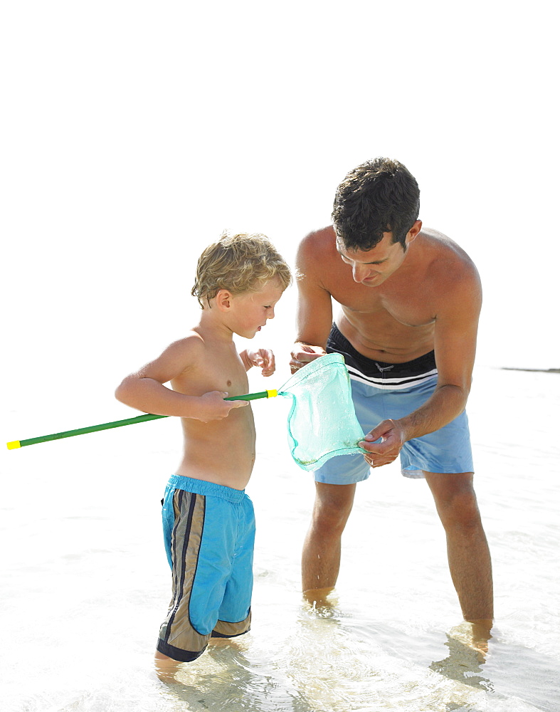 Father and son (6-8) in the surf holding fishing pole