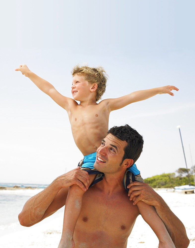 Son (6-8) sitting on father's shoulders on beach