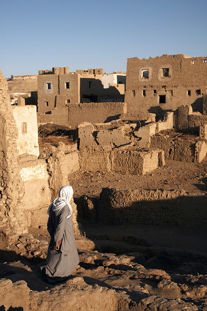 A man stands among the ruin of the mud-brick city of Al-Qasr, Dakhla Oasis, Egypt, North Africa, Africa