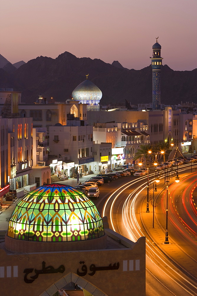 Elevated dusk view along the Corniche, stained glass dome of Mutrah Souq, colourful latticed buildings and Mutrah Mosque, Muscat, Oman, Middle East