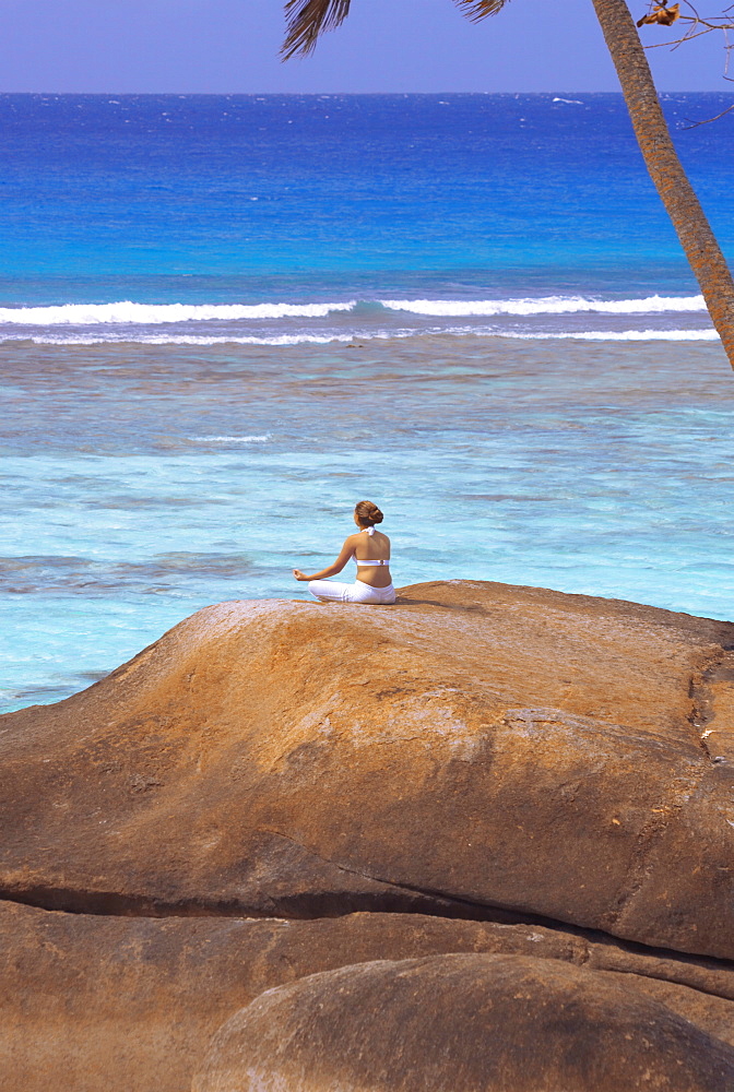 Young woman meditating on rock, Seychelles, Indian Ocean, Africa