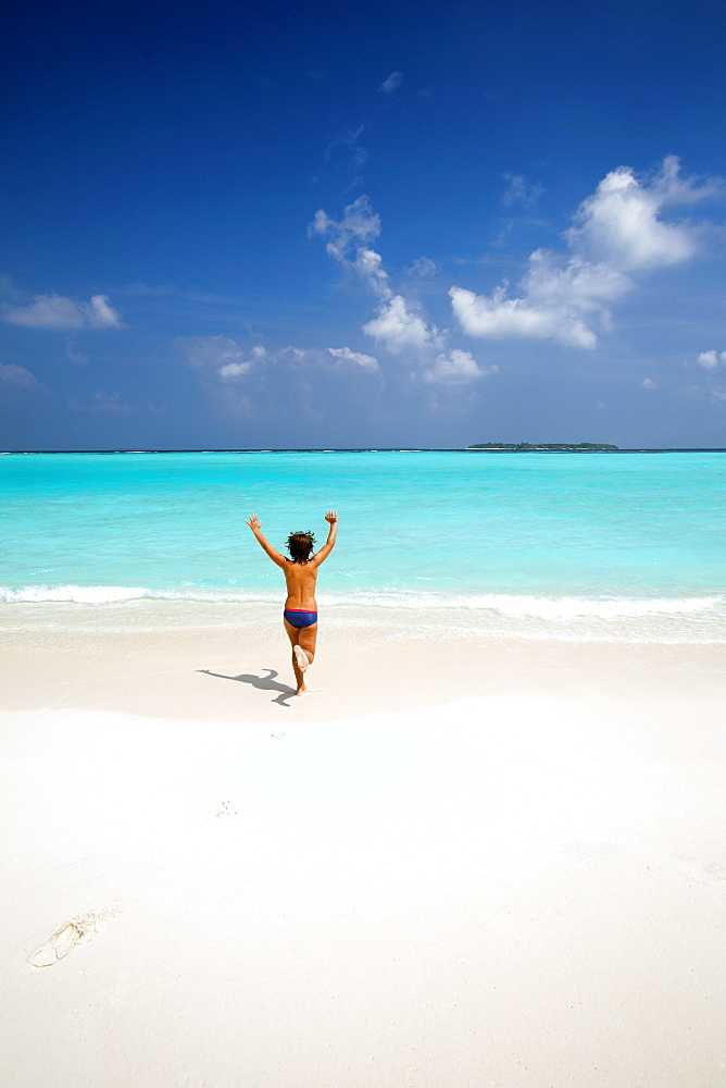 Boy running with arms raised on tropical beach, Maldives, Indian Ocean, Asia