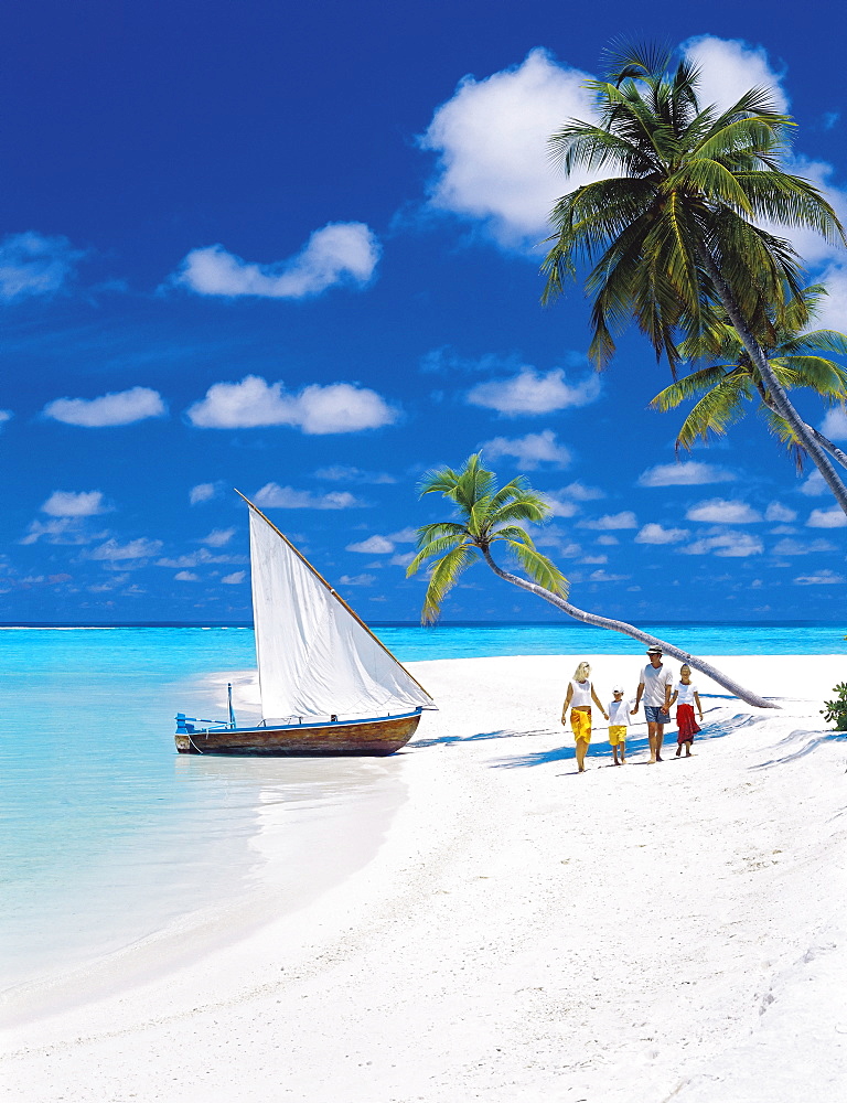 Family walking on a tropical beach by traditional dhoni, Maldives, Indian Ocean, Asia