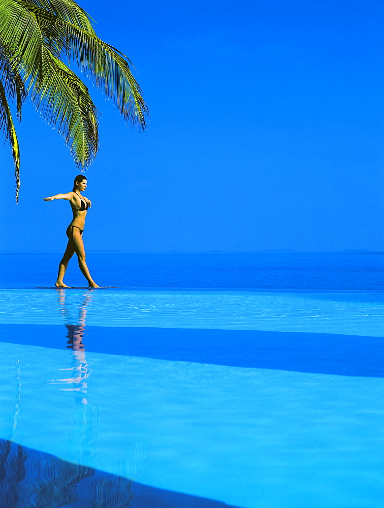 Woman balancing on edge of infinity pool, Maldives, Indian Ocean, Asia