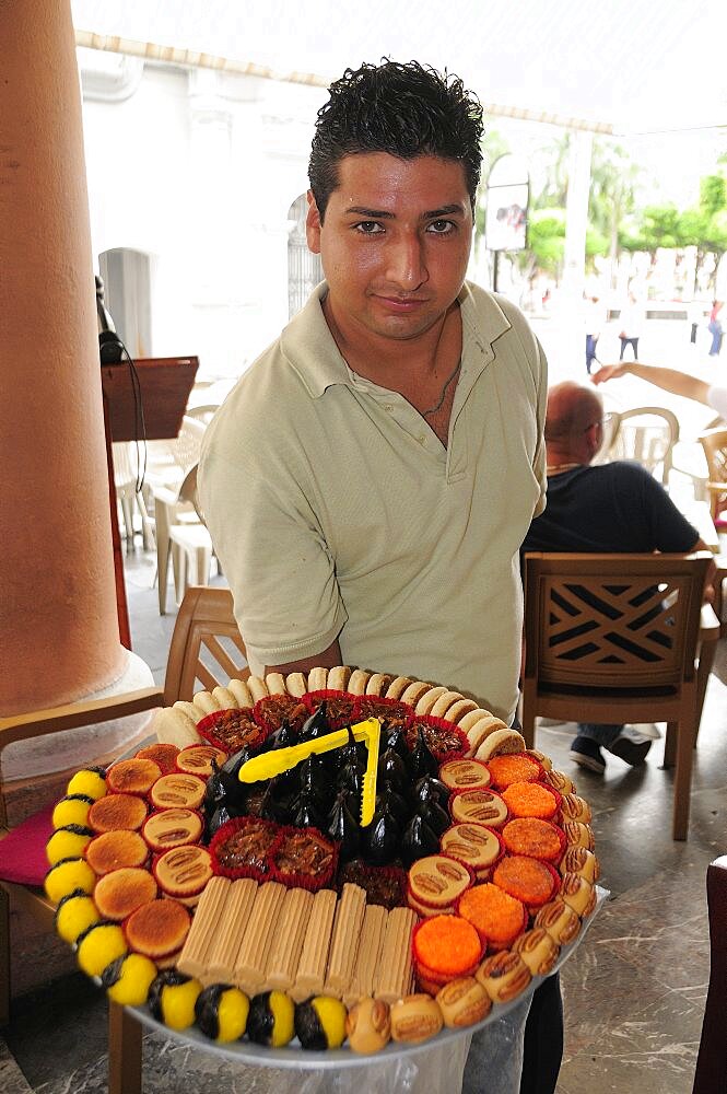 Mexico, Veracruz, Sweet seller in the Zocalo displaying large plate with variety of sweets.