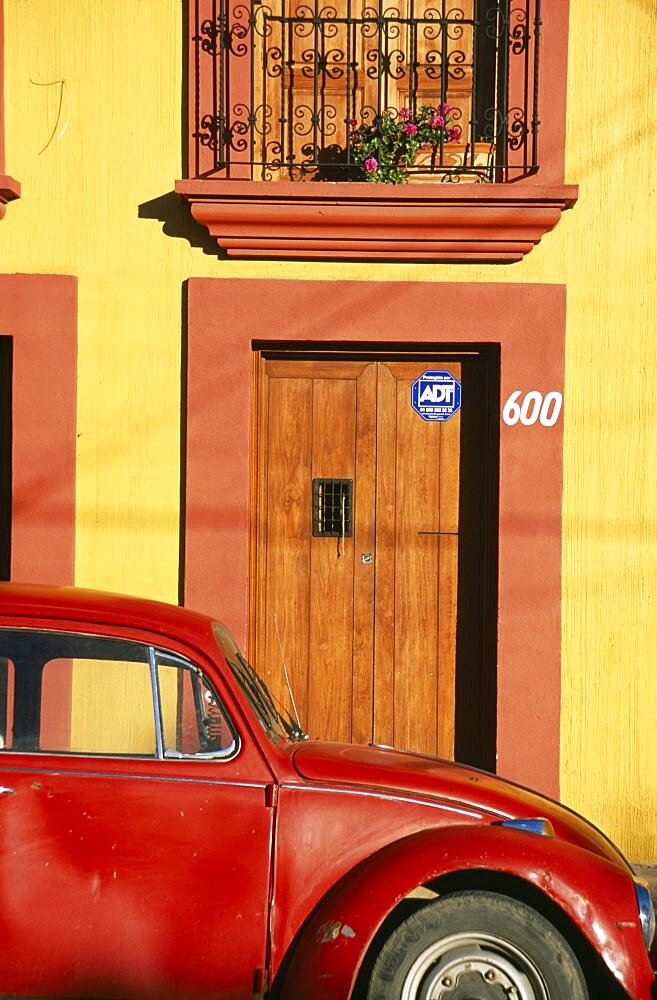 MEXICO Oaxaca Oxaca City Partly seen red volkswagon beetle outside yellow building with wooden door and window shutters in orange painted frames.