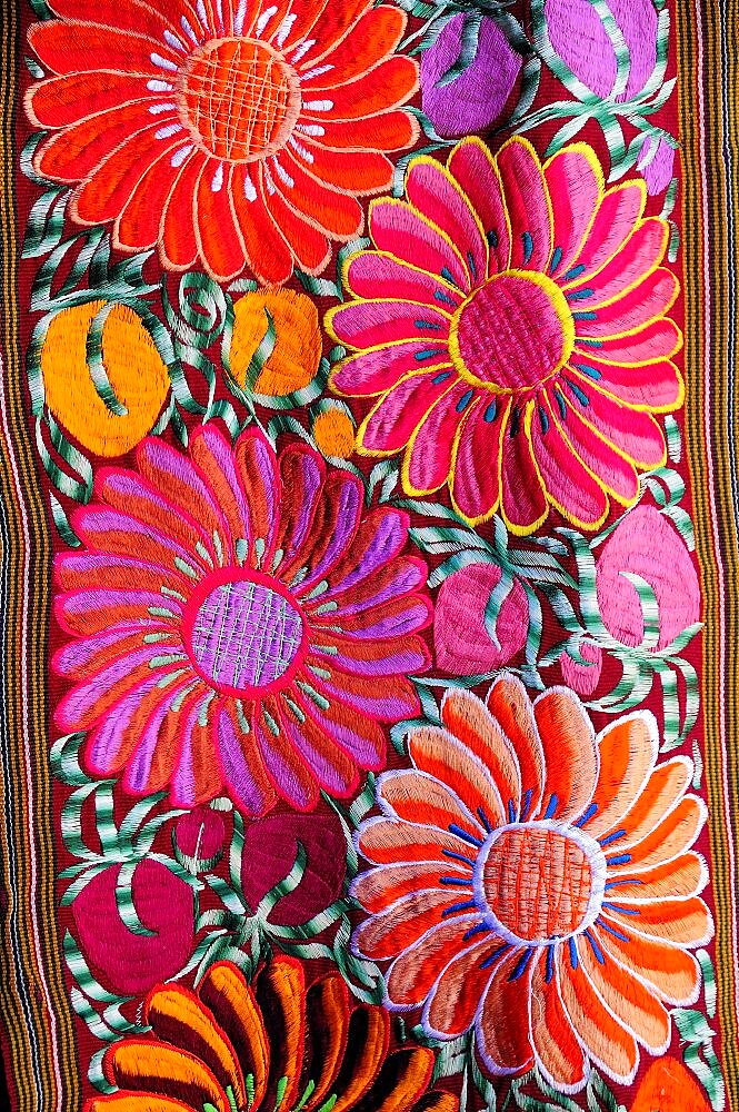 Mexico, Bajio, San Miguel de Allende, Detail of brightly coloured embroidered textile in arts shop with flower design in pink red and orange.