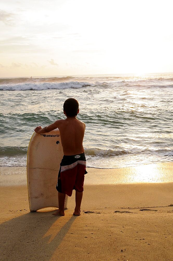 Mexico, Oaxaca, Puerto Escondido, Playa Zicatela Young body boarder standing on beach looking out to sea.