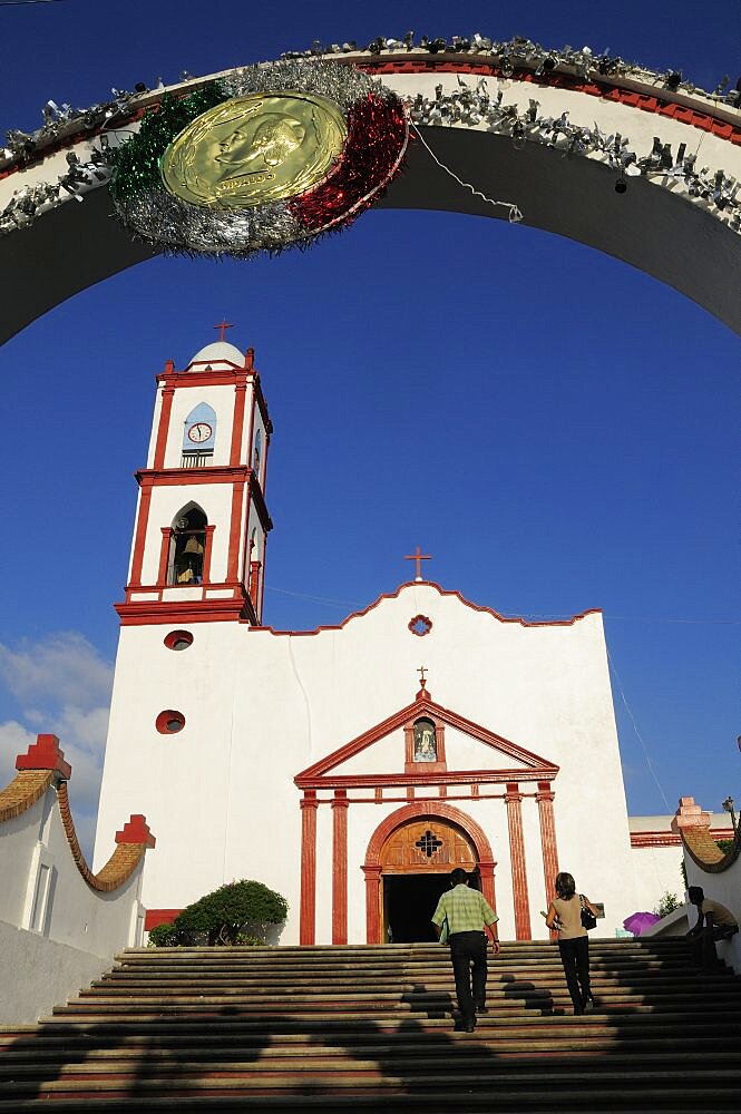 Mexico, Veracruz, Papantla, Cathedral de la Asuncion white and red painted exterior bell tower and steps to entrance framed by arch decorated for Independence Day celebrations.