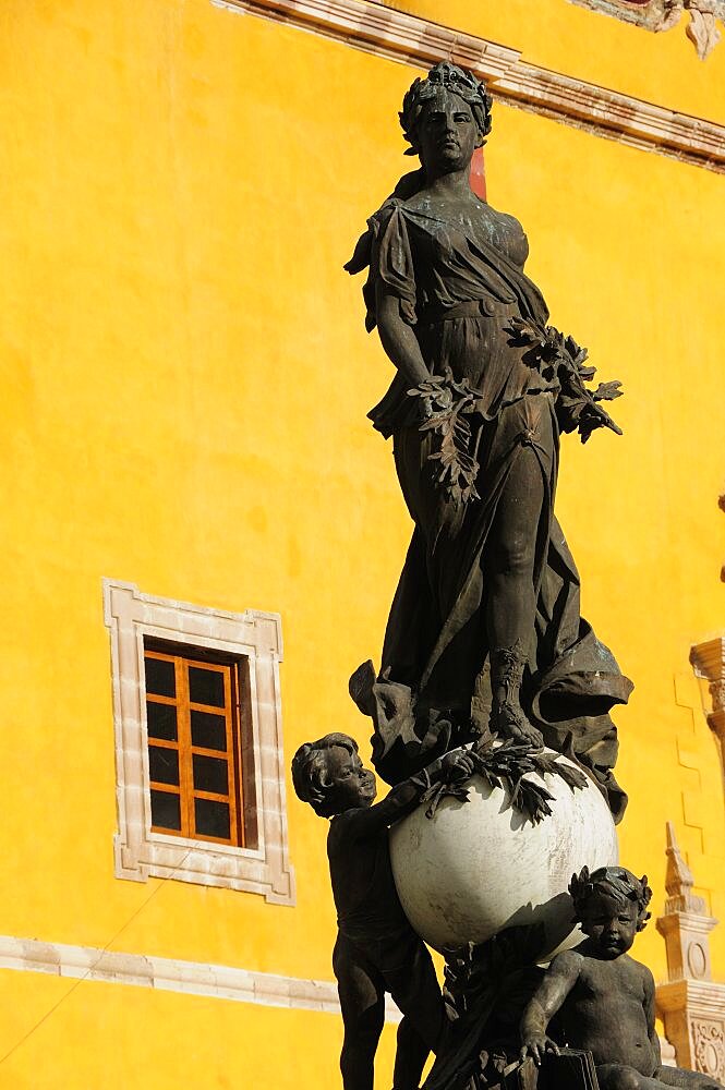 Mexico, Bajio, Guanajuato, Belle Epoque statue of Peace in Plaza de la Paz the Plaza of Peace also known as Plaza Mayor. With yellow exterior wall of Basilica Colegiata de Nuestra Senora de Guanajuato behind.