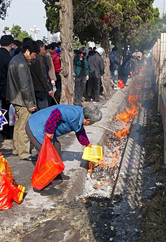 China, Jiangsu, Qidong, Qingming Festival when Chinese people honour their ancestors and deceased family members by visiting their graves or burial grounds to make offerings of fake bank notes and gold ingots which are then burned As the burning of offerings in not allowed inside most cemetries for safety reasons they are burned in the gutter outside.