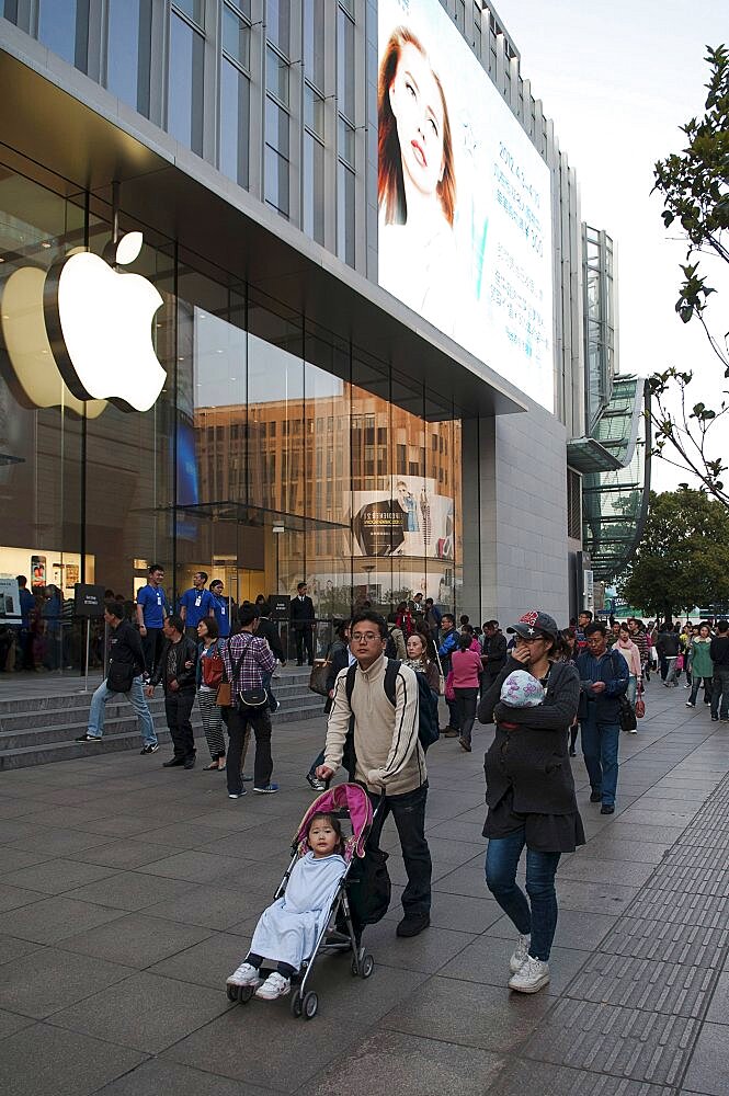 China, Shanghai, Modern young Chinese family with daughter in stroller and infant in sling stroll past the Apple store on Nanjing Lu Store staff and Security on steps at entrance evening light