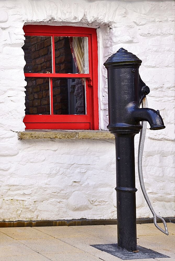 Ireland, North, Derry, Craft Village, Old water pump with small red window in background.