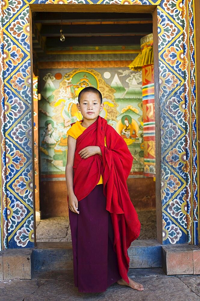 Bhutan, Chimi Lakhang, Young novice monk standing in doorway of Chimi Lakhang temple in the old capital.