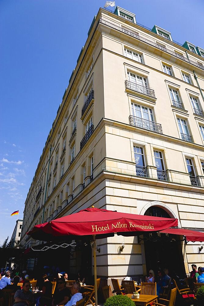 Germany, Berlin, Mitte, the rebuilt five star Hotel Adlon Kempinski on the corner of Unter den Linden and Pariser Platz with people at tables under umbrellas.