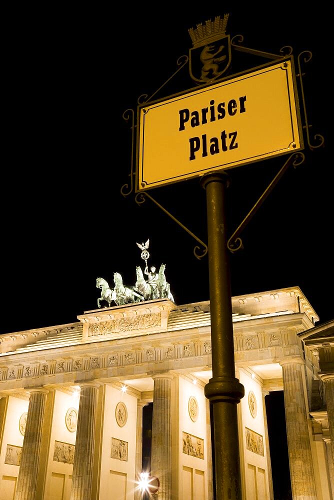 Germany, Berlin, Mitte, Brandenburg Gate or Brandenburger Tor and roadsign for Pariser Platz illuminated at night leading to Unter den Linden and the Royal Palaces with the Quadriga of Victory on top. The only remaining of the original 18 gates in the Berlin Customs Wall.