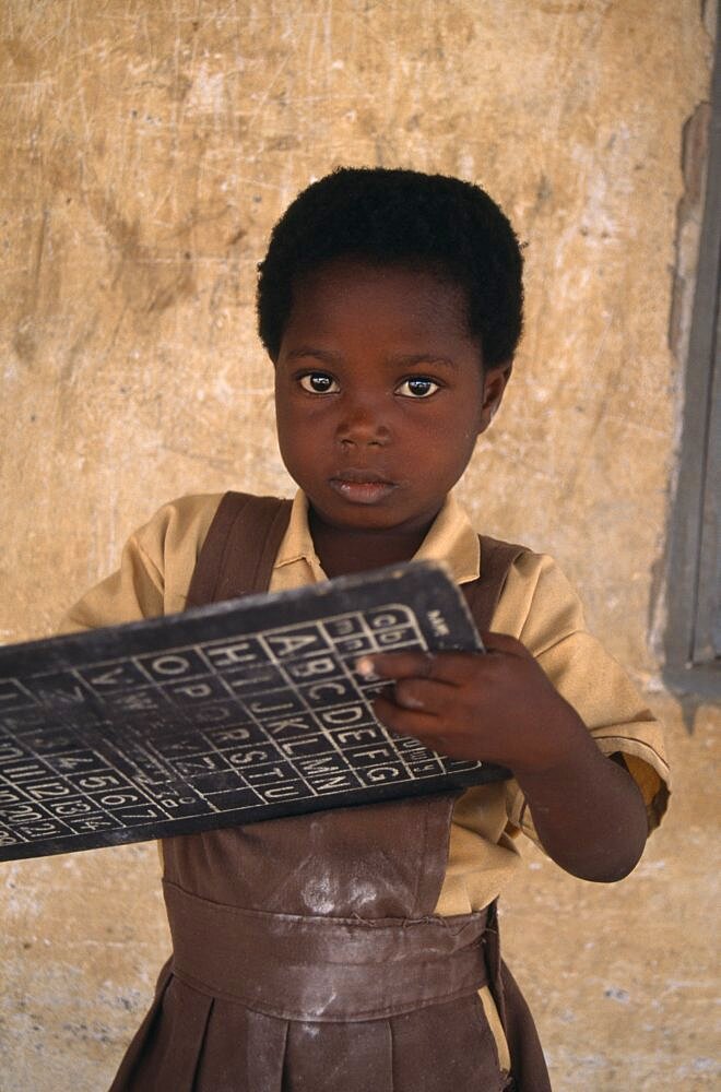 GHANA  Education Portrait of pupil from primary school in village near Accra holding small blackboard printed with alphabet and numbers.