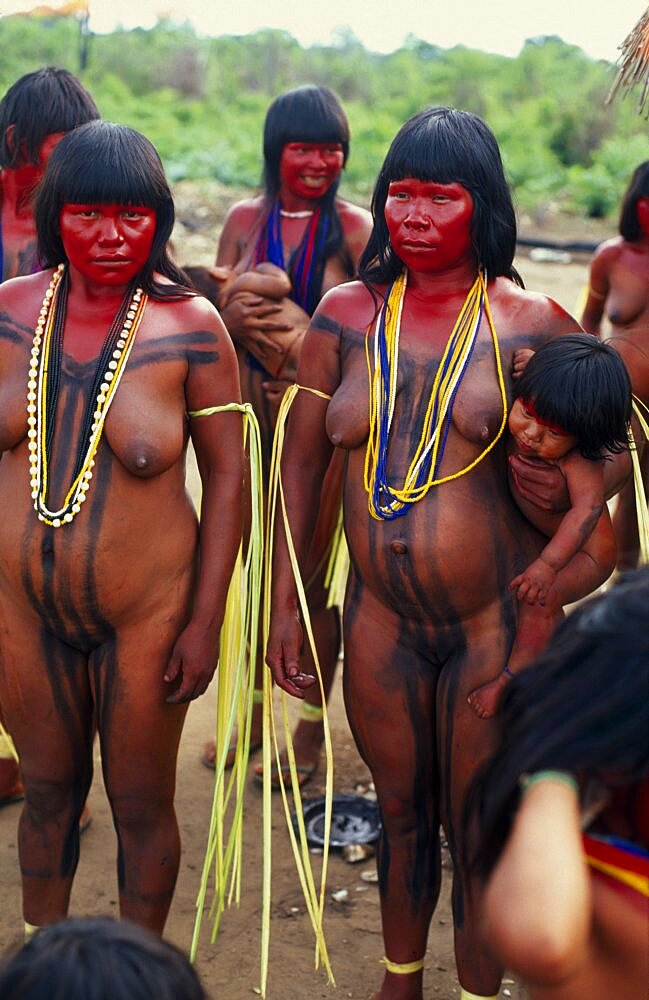 BRAZIL Mato Grosso Indigenous Park of the Xingu Panara women painted with red karajuru and wearing multi-strands of beads across upper body and long strips of plant fibres tied around upper arms in preparation for dance.  Formally known as Kreen-Akrore  Krenhakarore  Krenakore  Krenakarore  Amazon American Brasil Brazilian Female Women Girl Lady Indegent Kreen Akore Latin America Latino South America Female Woman Girl Lady Immature