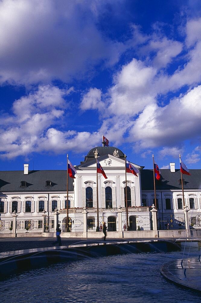 SLOVAKIA Bratislava Presidential Palace part view of exterior facade with flags. Circular fountain in the foreground passing people and Presidential guard either side of entrance.