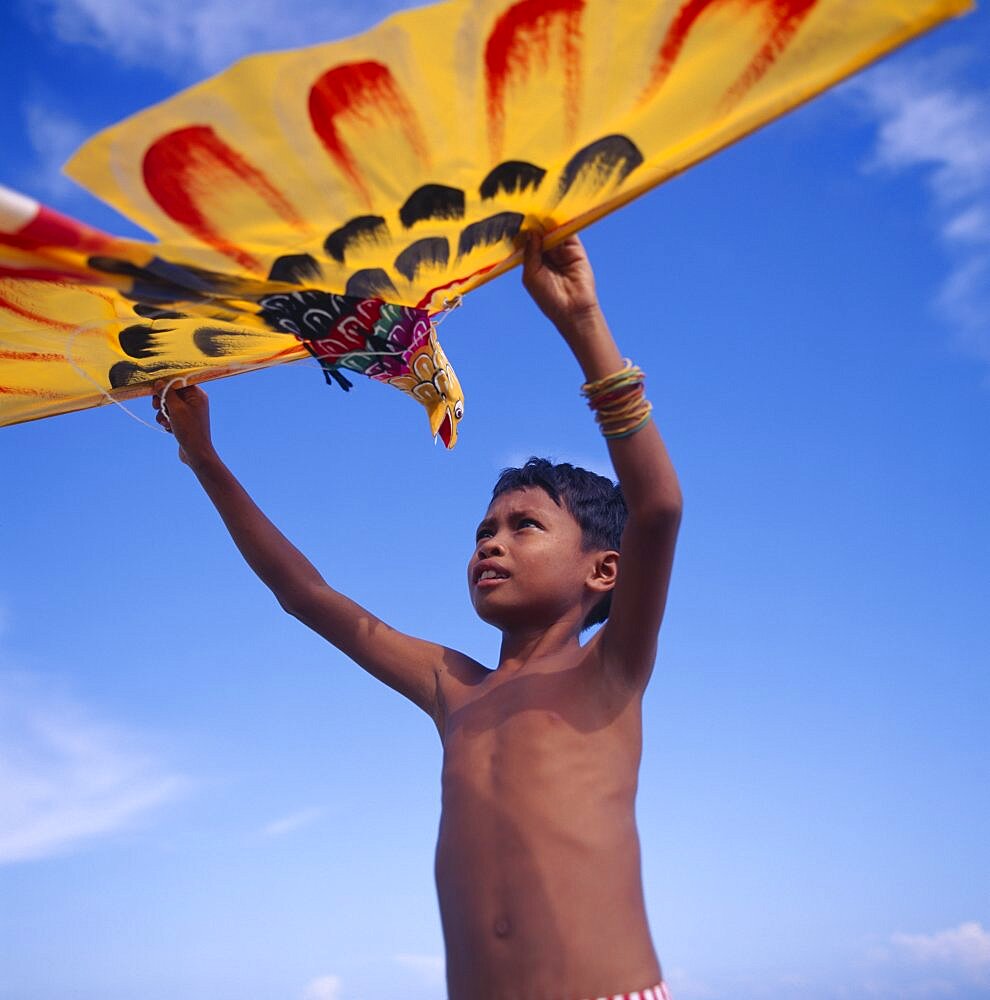 INDONESIA Lombok Timur Young boy holds up a yellow eagle shaped kite