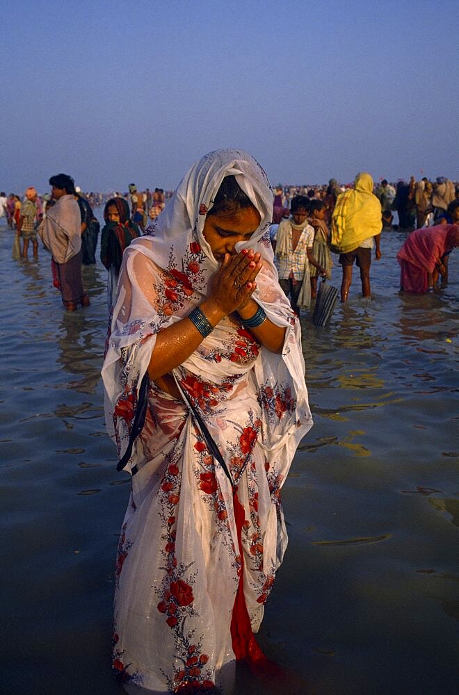 Woman pilgrim praying during three day Sagar bathing festival at point where the Ganges joins the sea, Other people in water behind her, Sagar Island, West Bengal, India