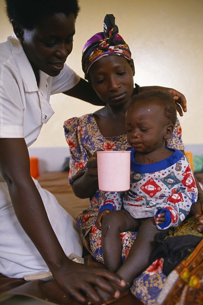 Nurse comforting mother with child with malaria in hospital in Orukinga refugee camp near the Rwandan border, Medical, Uganda