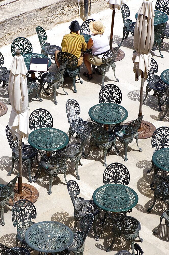 Couple of people sitting at a table amongst other wrought iron tables and chairs in a cafe below the Upper Barrakka Gardens overlooking Valletta Harbour, Valletta, Malta