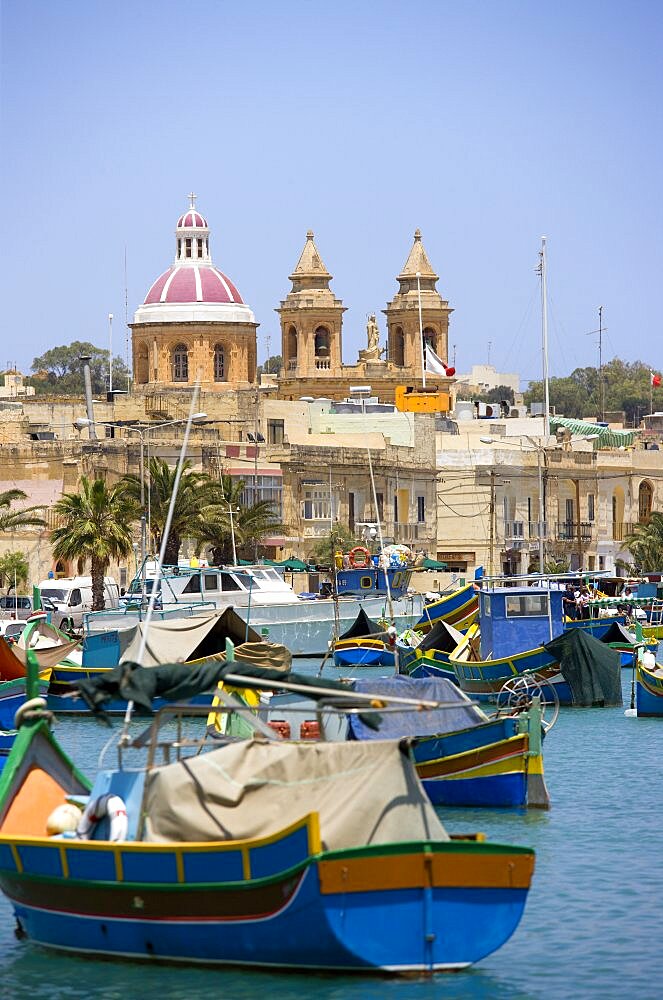 Fishing village harbour on the south coast with colourful Kajjiki fishing boats and the Church dedicated to Our Lady of the Rosary The Madonna of Pompeii, Marsaxlokk, Malta