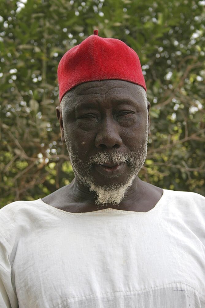 Tanji Village, Head and shoulders portrait of Muslim man with white trimmed beard wearing white shirt and red cap, Tanji, Western Gambia, The Gambia