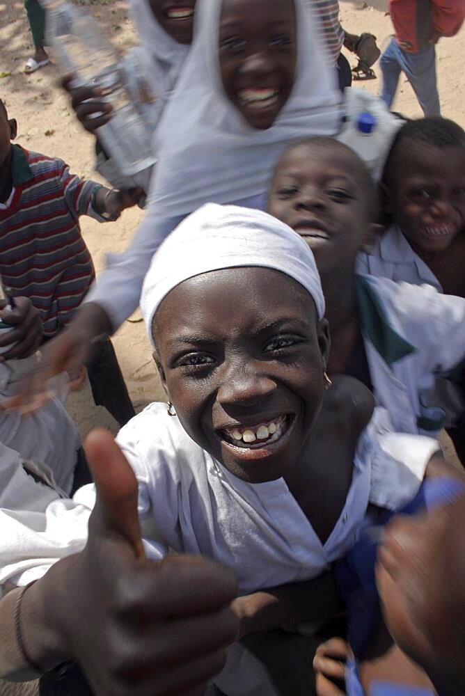 Tanji Village, Happy laughing children wanting to be photographed and trying to get the best position while having a break from lessons at the Ousman Bun Afan Islamic school, Child in centre foreground making a thumbs up gesture, Tanji, Western Gambia, The Gambia