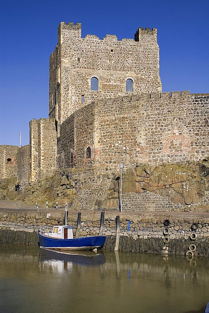 Ireland, County Antrim, Carrickfergus, Castle exterior with a boat moored in the foreground