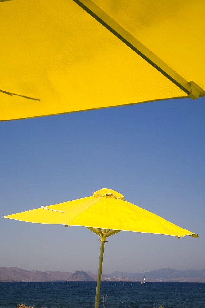 Greece, Dodecanese, Kos, bright yellow parasols on beach outside Kos Town, view towards distant coastline beyond