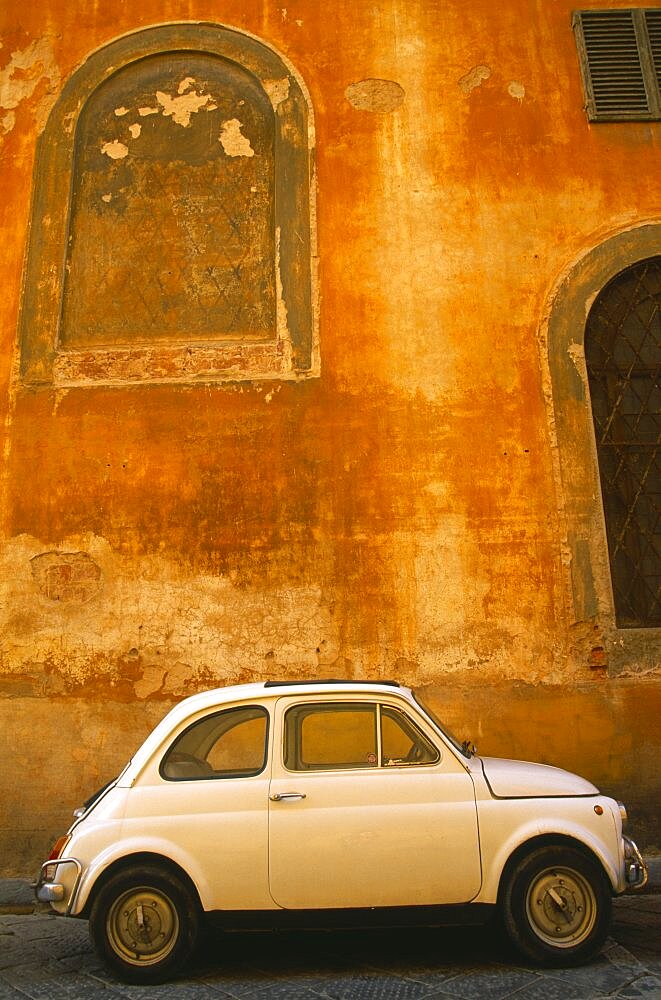 White Fiat 50 parked outside old building with faded ochre coloured plaster wall, Florence, Tuscany, Italy