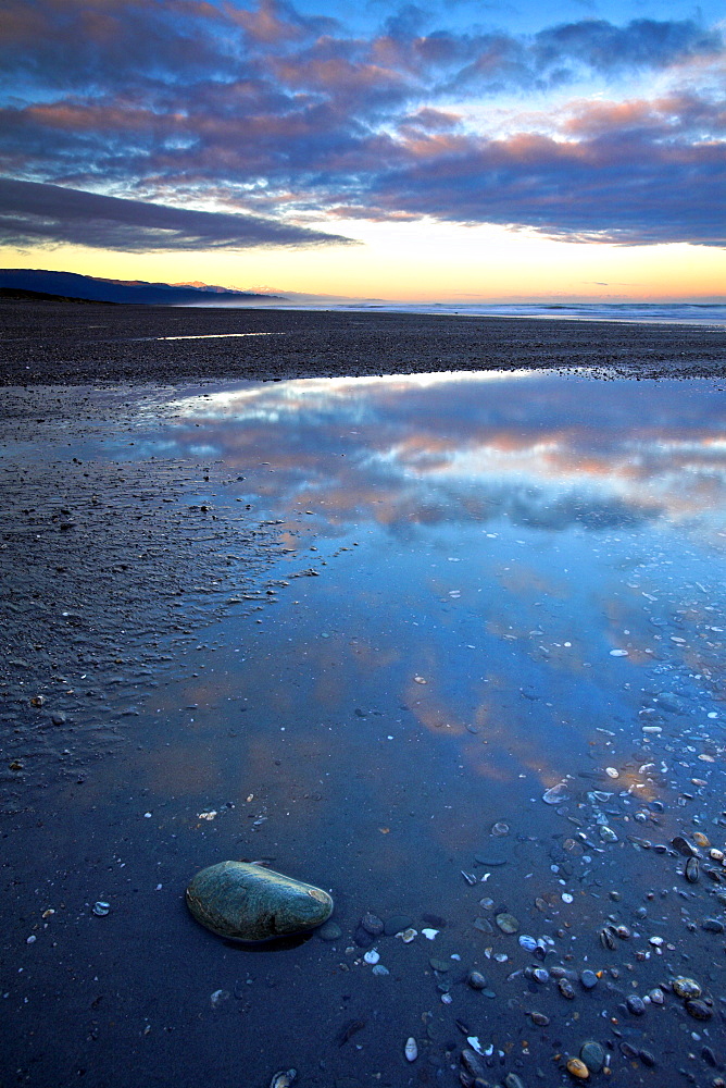 A remote west coast beach at dawn, the sunrise glistening on the Southern Alps mountain range in the distance, West Coast, South Island, New Zealand, Pacific