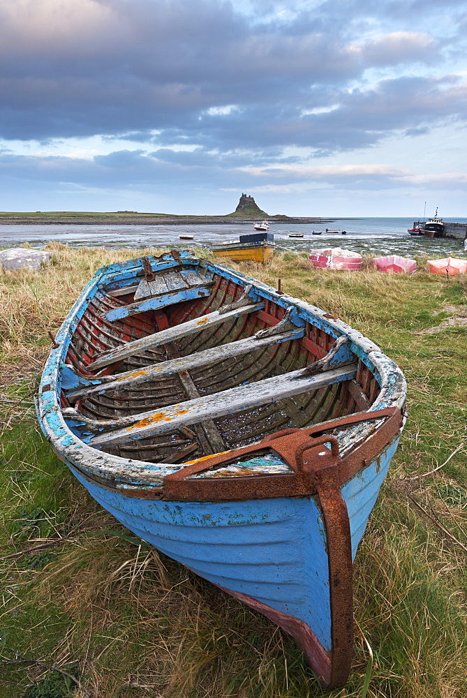 Old fishing boat pulled up on the shore at Holy Island, with the castle across the bay, Lindisfarne, Northumberland, England, United Kingdom, Europe 