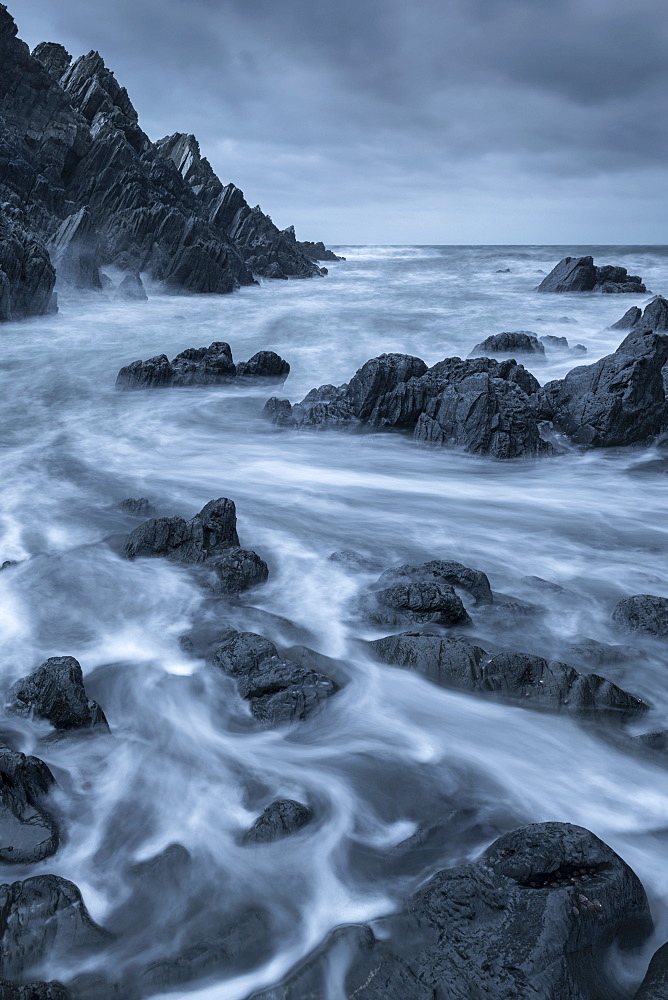 Swirling waves over dark rocks in a rugged North Devon cove, Devon, England, United Kingdom, Europe