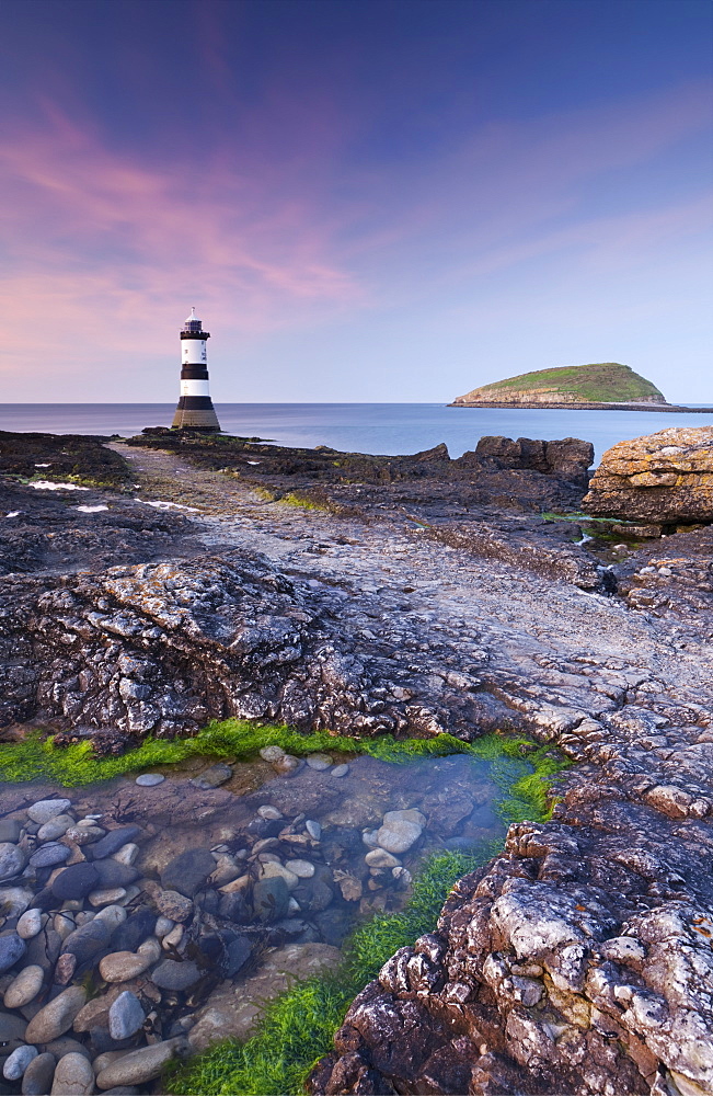 Twilight on the rocky Anglesey coast looking towards Penmon Point Lighthouse and Puffin Island, Anglesey, North Wales, Wales, United Kingdom, Europe