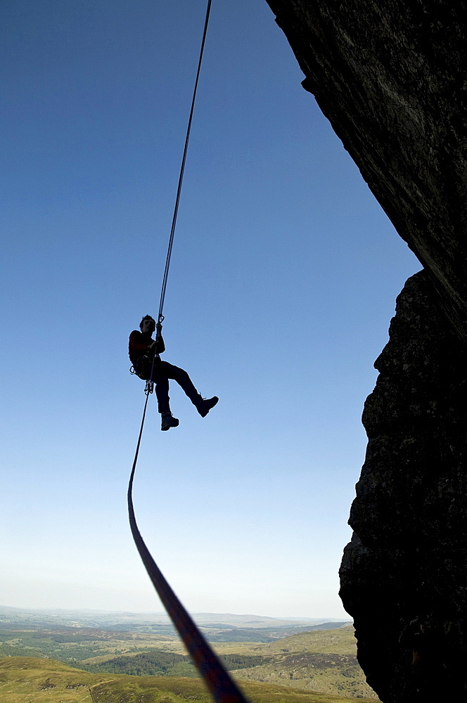 A climber makes a free-hanging abseil from a steep cliff in the Ogwen Valley, near Tryfan and Snowdon, Snowdonia, Wales, United Kingdom, Europe