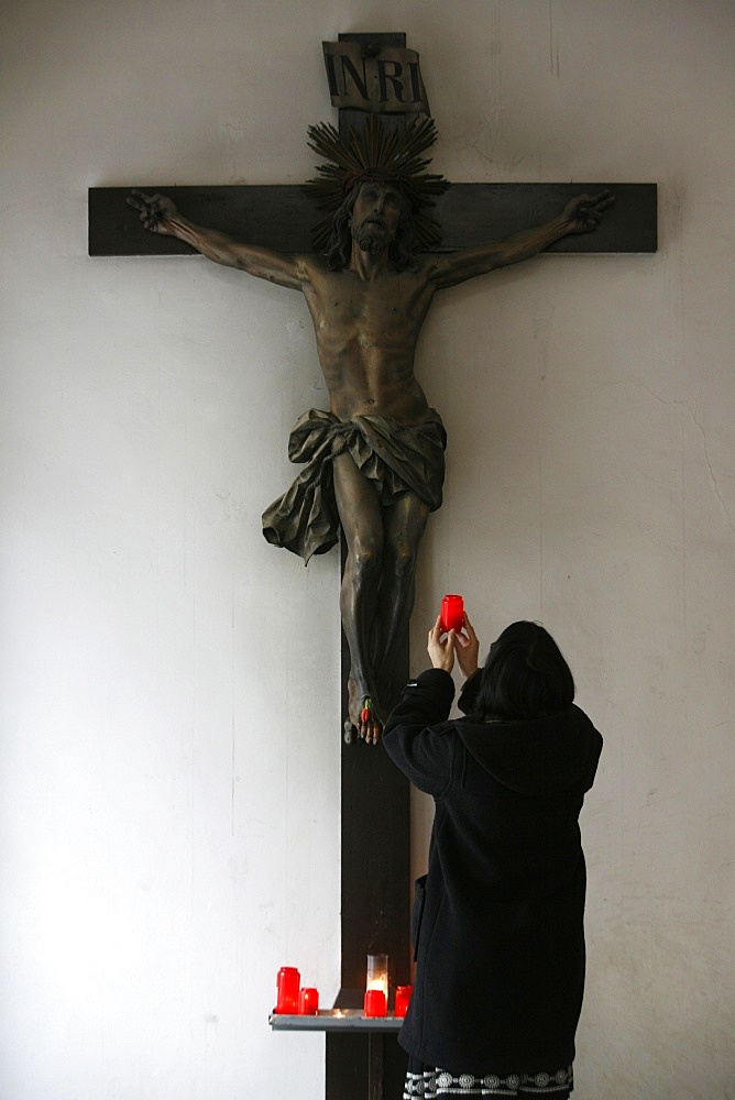 Woman offering candle and praying in front of Crucifix