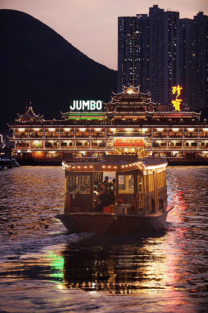 Ferry sailing towards Jumbo floating restaurant at dusk, Aberdeen harbour, Hong Kong, China, Asia