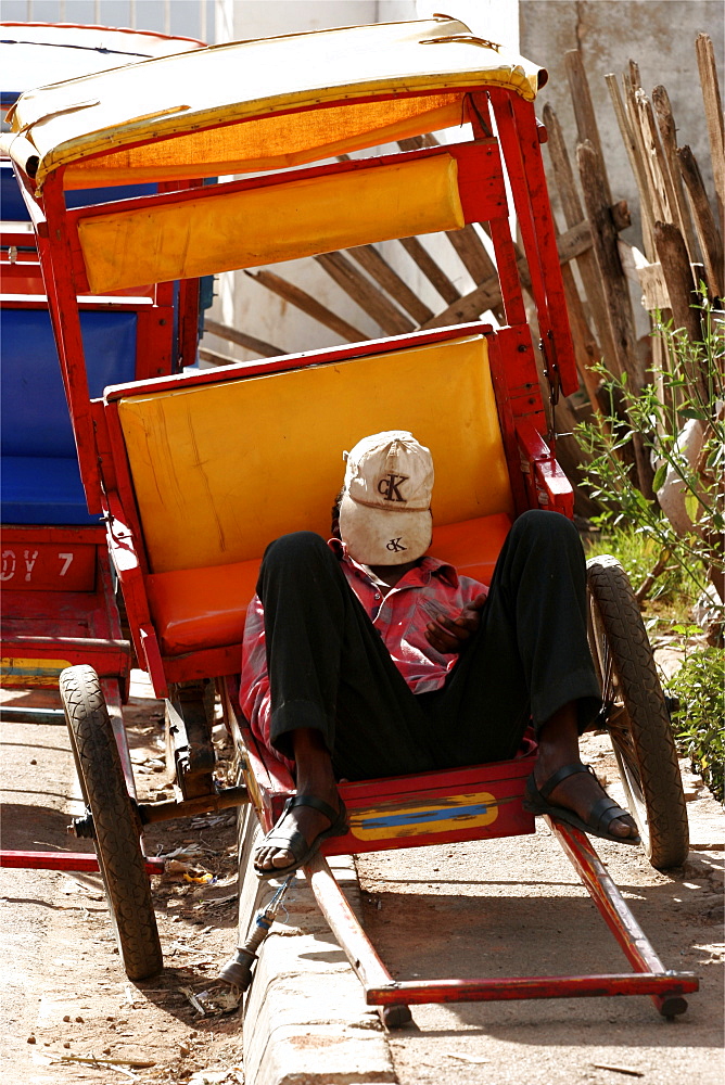 A pousse-pousse driver has a rest  on a street in Antsirabe, Madagascar, Africa