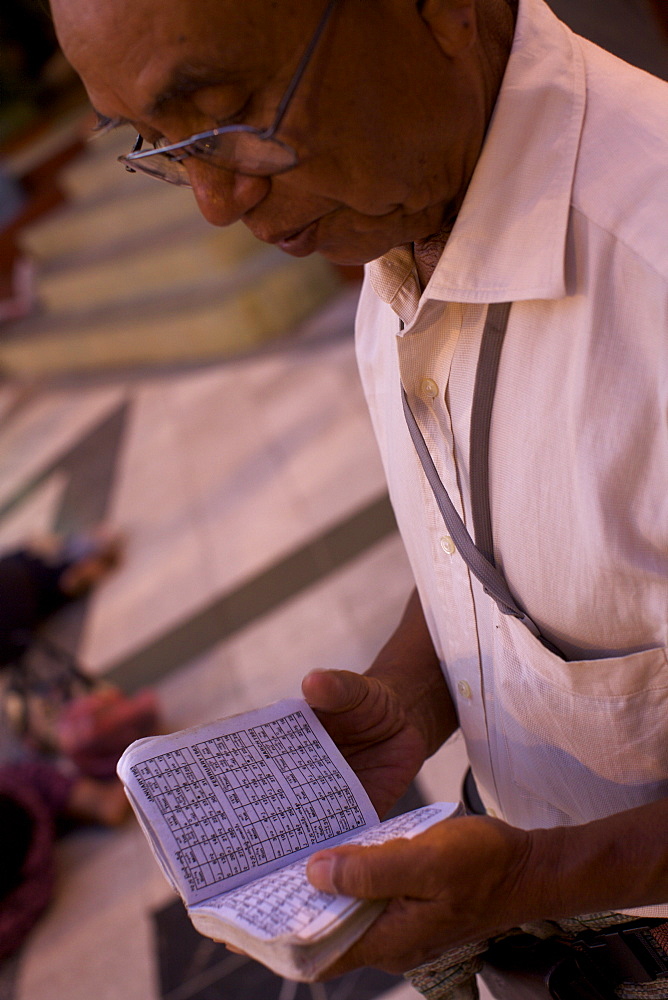 A man reading a Buddhist calendar at the Paya Shwedagon temple in Yangon, Myanmar (Burma), Asia