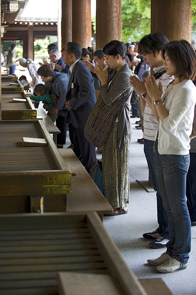 Worshippers praying in front of offertory boxes at main hall of Meiji Jingu shrine in Tokyo, Japan, Asia