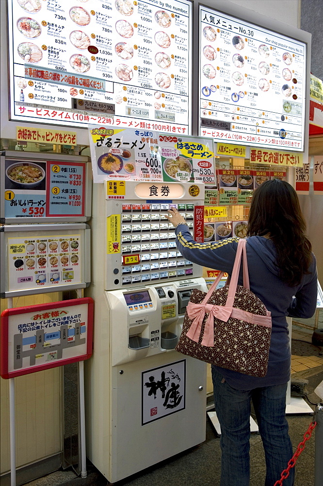 Woman purchasing meal tickets from a vending machine at a restaurant in Dotonbori, Osaka, Japan, Asia