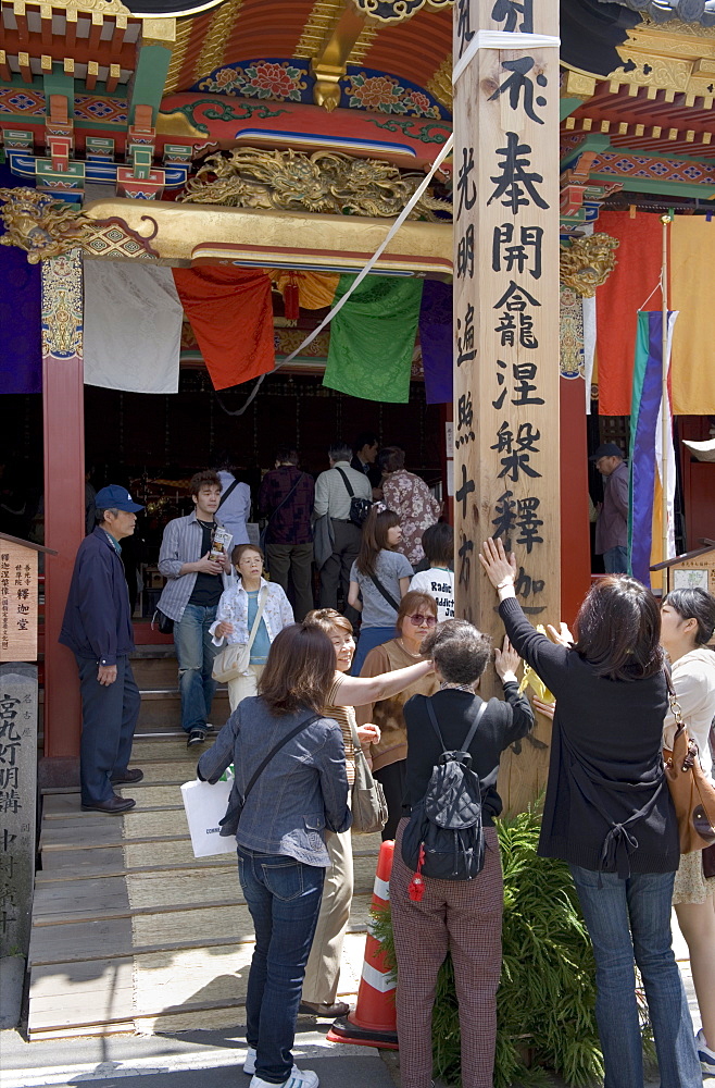 Worshippers touching a wooden obelisk for inspiration at a sub temple of Zenkoji Temple, Nagano City, Japan, Asia