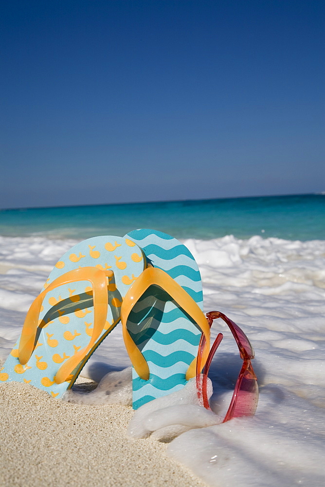 Two mismatched beach flip-flops with red sunglasses in the surf on a Caribbean beach, West Indies, Central America