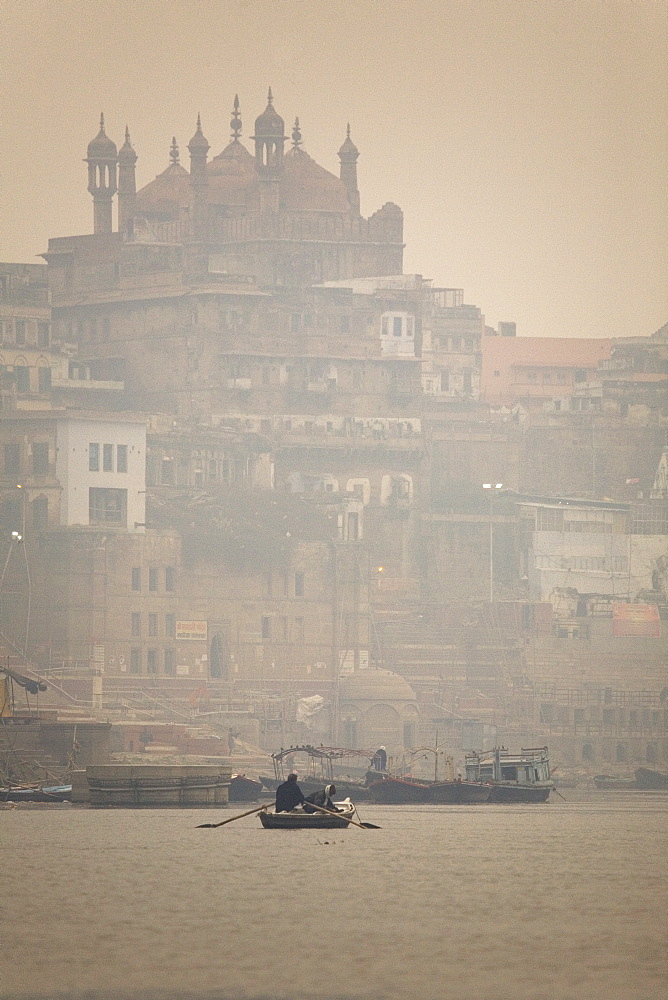 A boat is rowed on a typically foggy morning in the Ganga (Ganges) River at Varanasi, Uttar Pradesh, India, Asia